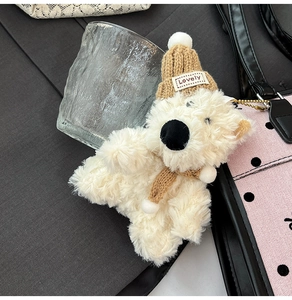 Detail of a white plush polar bear keychain with brown knit hat and scarf on a polka dot bag