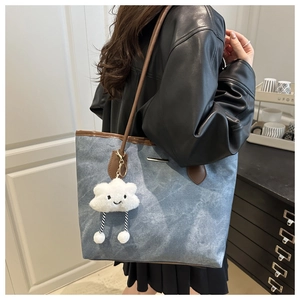 Détail du sac fourre-tout en denim bleu avec lanières en cuir brun et pendentif
