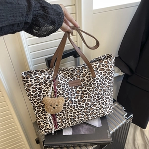 Leopard print tote bag with brown handles and plush bear charm on travel suitcase