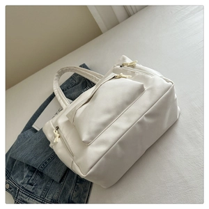 Detail of a white canvas tote bag featuring an external pocket and side zipper with cord