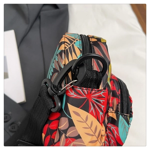 Detail of colorful leaf print crossbody bag with black D-ring and nylon strap