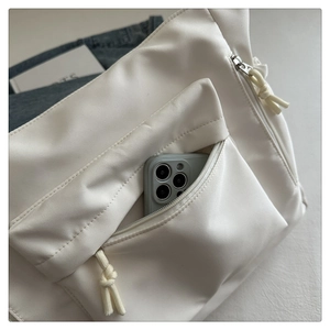 Detail of front zipper pocket on white tote bag showing storage for a large smartphone