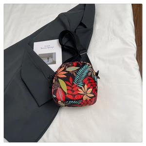 Detail of crossbody bag with colorful leaf print on a dark grey blazer backdrop