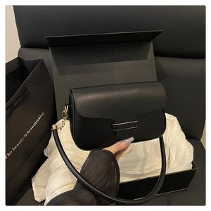 Détail d'un sac bandoulière en cuir noir avec boucle dorée dans un coffret cadeau luxe