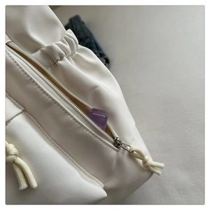 Detail of white nylon tote bag side zipper pocket with woven drawstring and purple accessory
