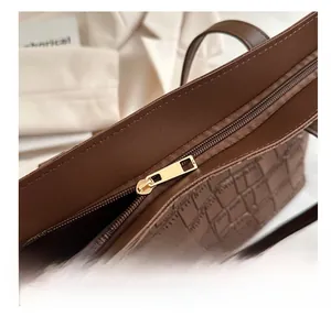 Close-up of golden metal zipper and crocodile embossed texture on brown tote bag