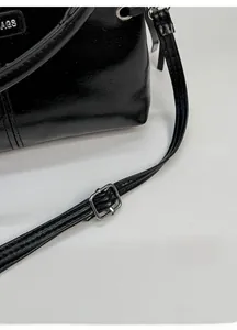 Details der silbernen Schnalle und des AGS-Metalllogos an der glänzenden schwarzen Tasche