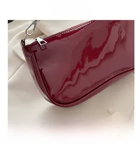 Close-up of red patent leather baguette bag featuring silver zipper and metal hook hardware