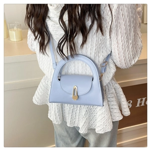 Detail view of a light blue leather handbag with gold buckle and adjustable strap