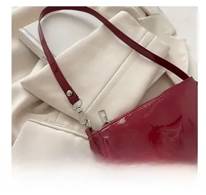 Detail of red patent leather shoulder bag showing glossy texture and silver metal hardware