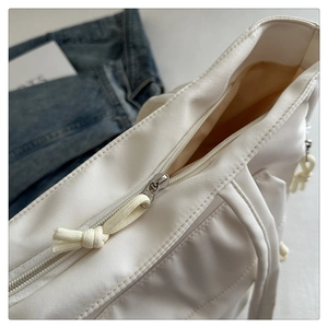 Detailed close-up of zipper closure and woven cord pull on a white nylon tote bag