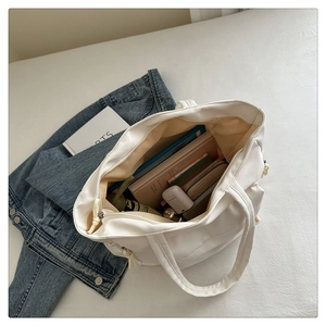 Detail view of large white tote bag interior holding a tablet, books, and daily essentials
