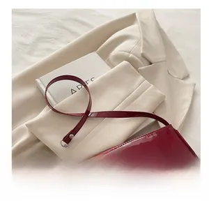 Glossy burgundy patent leather baguette bag styled on a beige blazer with art book