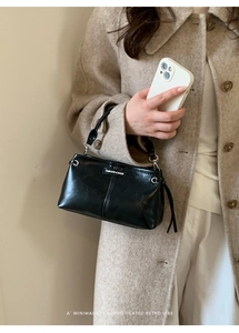 Detail einer schwarzen Lederhandtasche mit silbernen Beschlägen, getragen von einem Modell