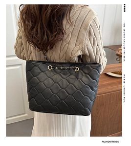 Close-up of black quilted tote bag with chain strap worn by a model in a cozy indoor setting