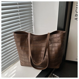 Detailed view of brown crocodile-embossed tote bag with slender straps in a modern setting