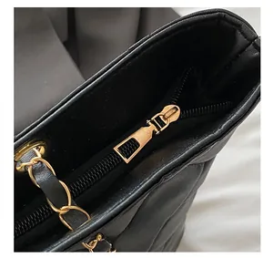 Close-up of golden zipper closure and leather chain strap on black quilted tote bag