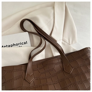 Détail d'un sac cabas marron foncé à texture crocodile sur une veste de costume beige