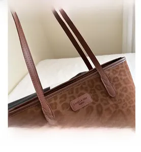 Close-up of leopard print suede tote bag featuring a leather logo patch and stitched detail