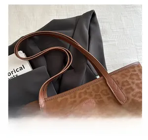 Detail of leopard print tote bag with brown leather handles and brand logo patch