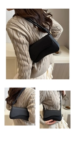 Detail of black pebbled leather baguette bag with wavy curved flap and knotted shoulder strap