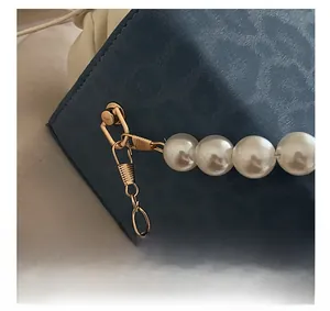 Detailed close-up of golden hardware clasp and elegant pearl chain on a navy blue bag