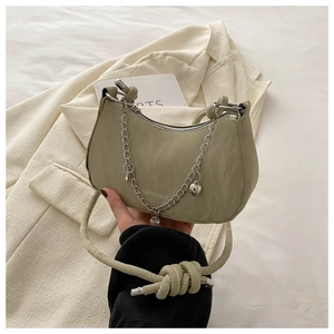 Detail of light green crescent shoulder bag featuring metal chain and heart pendant