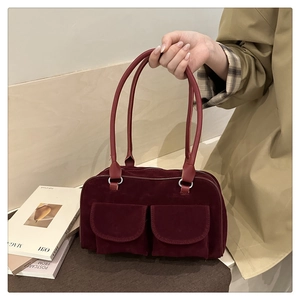 Detail of burgundy suede handbag featuring double front flap pockets and slim handles