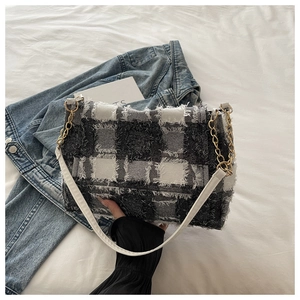 Detail of black and white plaid tweed shoulder bag with fringe edges and gold chain strap