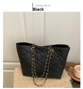 Detail of black quilted leather tote bag with gold chain strap on soft plush surface