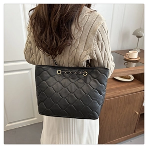 Detailed back view of a black quilted tote bag with chain strap worn in a home setting