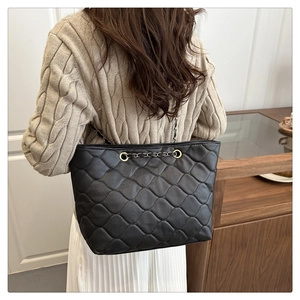 Close-up of black quilted tote bag with retro gold chain strap worn by a model