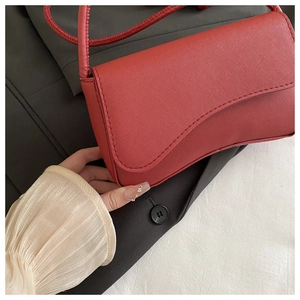 Detail van rode baguette-tas met Saffiano-textuur en golvende flap in de hand vast