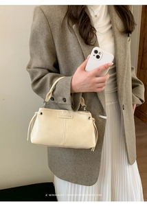 Detail der cremefarbenen PU-Lederhandtasche mit seitlichem Kordelzug und Metallschnalle