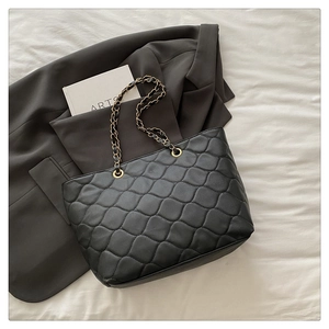 Detail of black quilted tote bag featuring gold chain straps and rhombic pattern