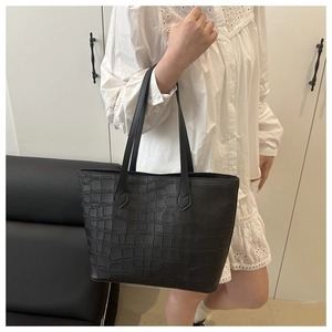 Detail of black crocodile embossed tote bag styled with white embroidered dress