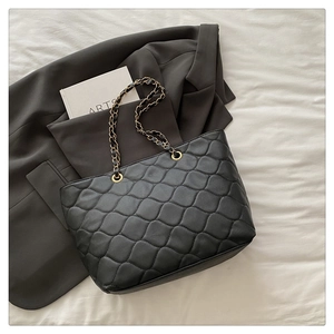 Close-up of quilted tote bag with gold chain strap on a stylish gray suit background