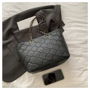 Close-up of black quilted tote bag with chain strap styled with art book and blazer