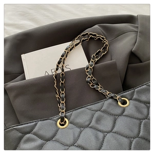Macro detail of black quilted tote bag with gold grommets and leather-woven chain strap