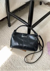 Detailansicht der schwarzen glänzenden Ledertasche mit Metall-Logo auf beigem Teppich