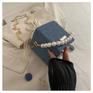 Close-up of blue cube bucket bag with pearl handle, chain strap and white drawstring top