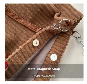 Detailed close-up of brown corduroy fabric with magnetic snap button and metal ring chain