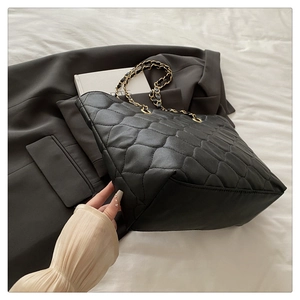 Macro shot of wavy quilted texture and gold chain strap on a black faux leather tote bag