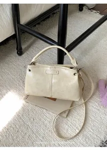 Detailansicht der cremefarbenen Ledertasche mit Logo-Plakette auf Teppichboden