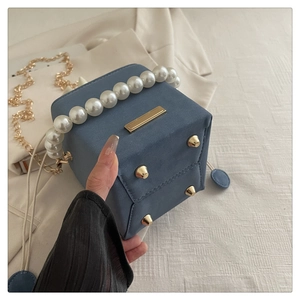 Detail of grey-blue box clutch bag showing pearl handle and bottom protection rivets