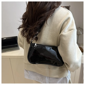 Close-up of black glossy patent leather shoulder baguette bag with silver zipper detail