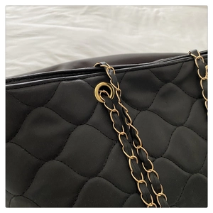Detail of black quilted tote bag with golden metal chain strap and luxury wave texture