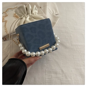 Detail of navy blue crossbody bag with oversized pearl handle and gold chain strap