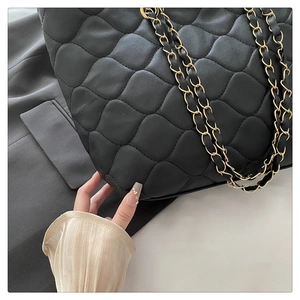 Detailed macro view of black quilted shell texture and gold chain strap on tote bag