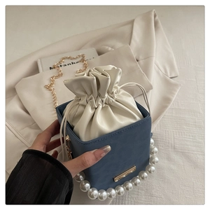 Close-up of blue square bucket bag with pearl handle and golden chain strap